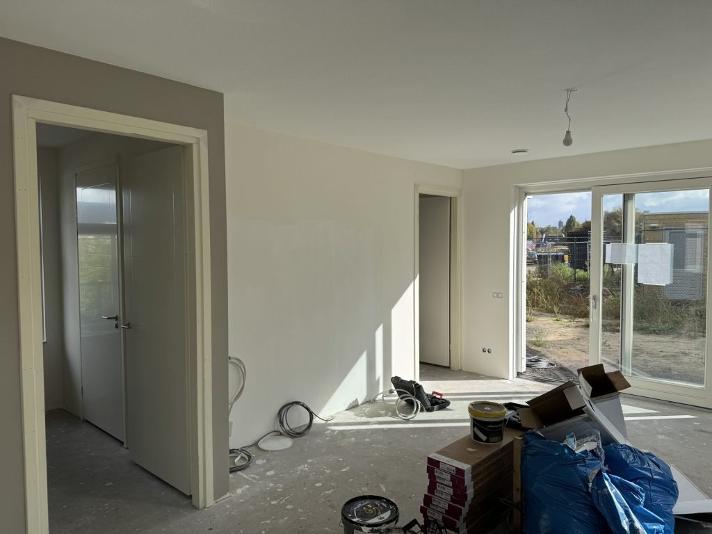 Woonkamer tijdens de afwerking, met verfemmers, dozen en materiaal op de vloer
