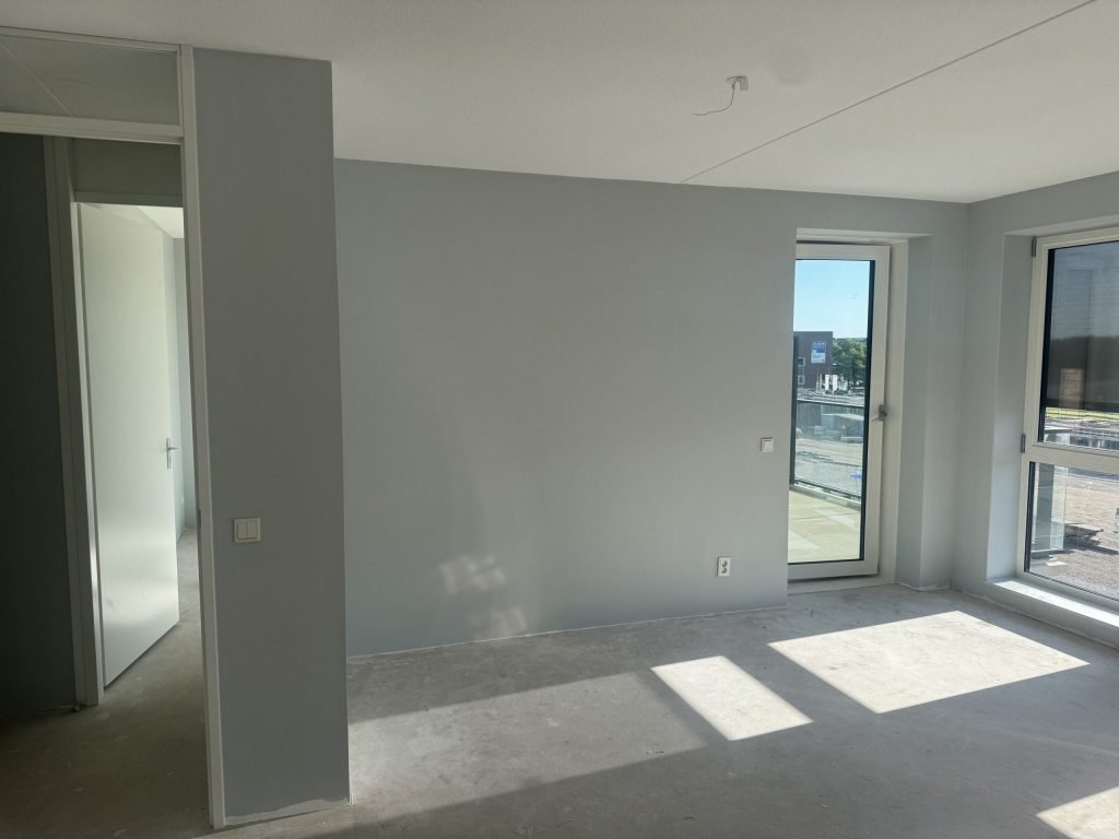 Afgewerkte nieuwbouwkamer met egale lichtgrijze wanden en zon op de vloer