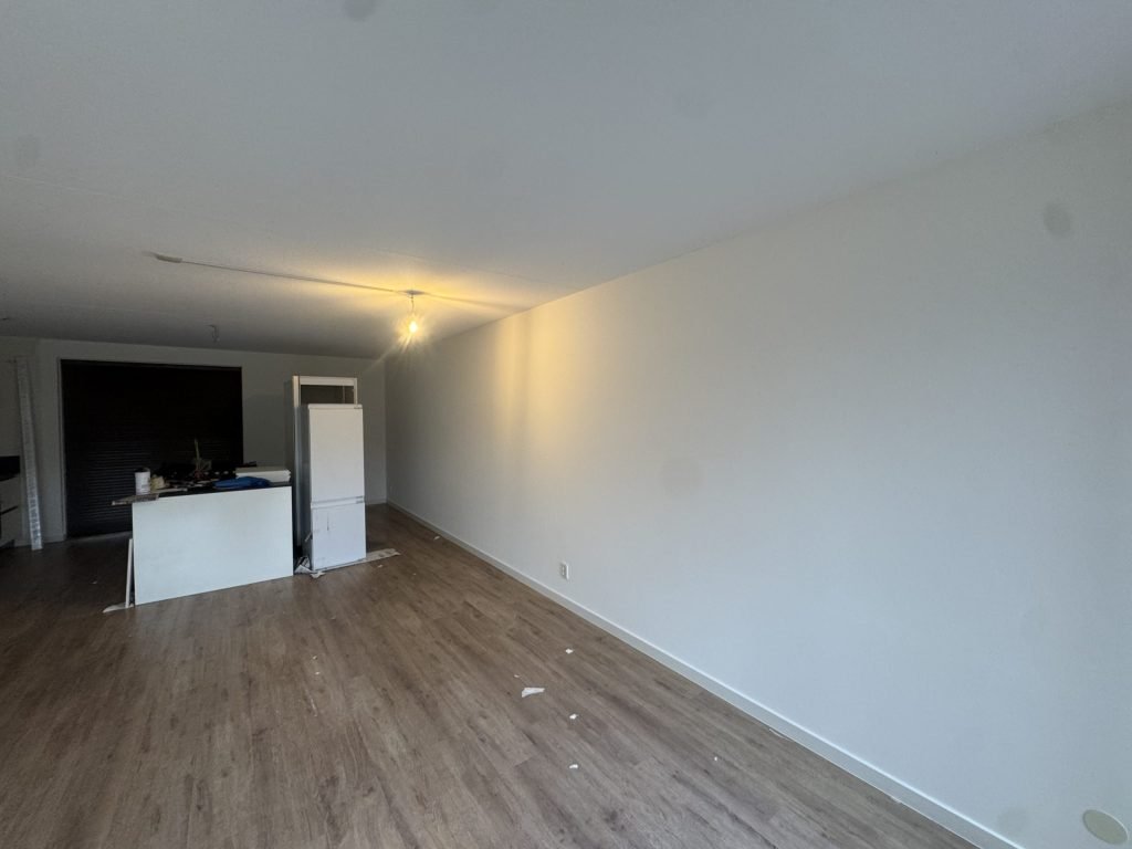 Afgewerkte woonkamer met gladde witte wanden, laminaat en een keukenblok