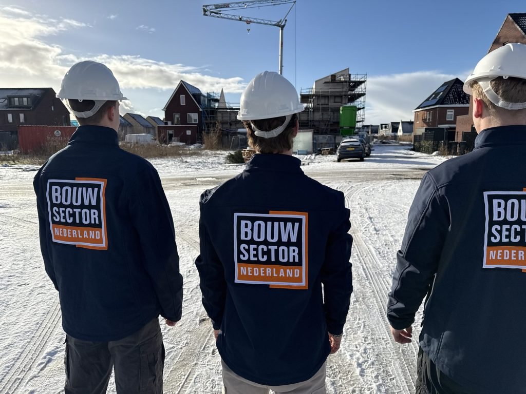 Drie vakmensen van Bouwsector Nederland met witte helm op een besneeuwde nieuwbouwplaats